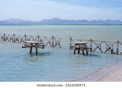 Tranquil coastal scene with rustic wooden fences and tables in shallow water - Powered by Shutterstock