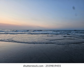 A tranquil coastal sunset captures the sun as it dips below the horizon, casting a soft pink glow over the calm ocean waves. The serene sky blends pastel hues of lavender, blue, and peach, reflecting  - Powered by Shutterstock