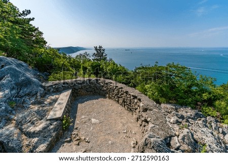 A tranquil coastal viewpoint features a stone bench and wall overlooking serene waters on the Gulf of Trieste in Italy