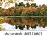 Tranquil and colorful autumn scene in New England. Reflection of vibrant fall foliage on calm surface of Mill Pond in Littleton, Massachusetts. 