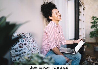 Tranquil Ethnic Woman In Trendy Striped Shirt With Closed Eyes Using Laptop While Sitting Cross Legged On Couch At Home 