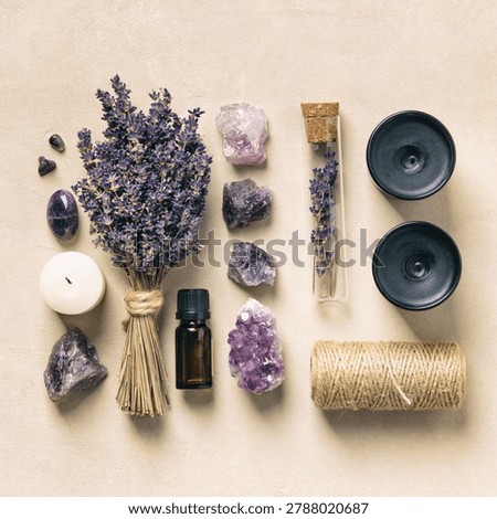 A tranquil flat lay scene featuring a amethyst crystals, amber glass essential oil bottles, a burning candle, a feather, and dried lavender sprigs, all arranged on a light stone background. 