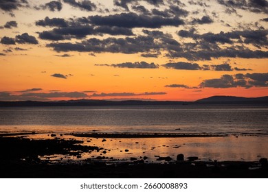 A tranquil horizontal landscape captures the dramatic colors of a sunset over the beach at Port Seton, Scotland