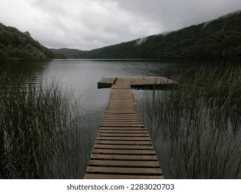 A tranquil lake framed by lush greenery and majestic mountains in the background. A wooden pier juts out into the w - Powered by Shutterstock