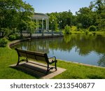 Tranquil lake landscape with a bench,  water reflections, and Bandstand Pavillion on Roosevelt Lake at Roger Williams Park in Providence, Rhode Island