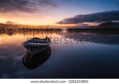 A tranquil lake reflects a pink sky at dawn, the beauty of nature enhanced by a small row boat in its midst.