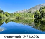 A tranquil lake surrounded by lush greenery, reflecting the clear blue sky and majestic San Bernardino Mountains.