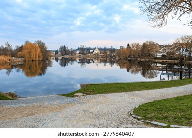 Tranquil lakeside scene with reflection of trees and houses at dusk.