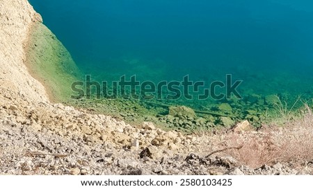 Tranquil lakeside view showcases clear blue water touching rocky shore, ideal for relaxation or eco tourism promotion