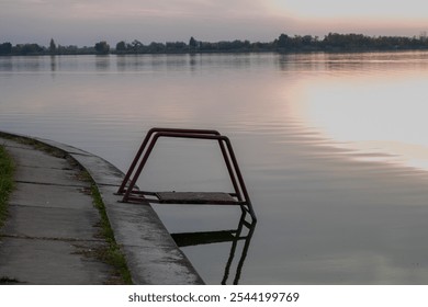 Tranquil lakeside view at sunset with a submerged handrail, symbolizing isolation and introspection, ideal for mental health themes - Powered by Shutterstock