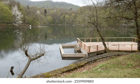 Tranquil lakeside view with a wooden deck surrounded by lush greenery and calm waters. - Powered by Shutterstock