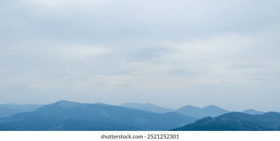 A tranquil landscape of many mountain ranges disappearing into the distance under a smoky, overcast sky. The layers of hills transition from darker tones in the foreground to lighter tones. - Powered by Shutterstock