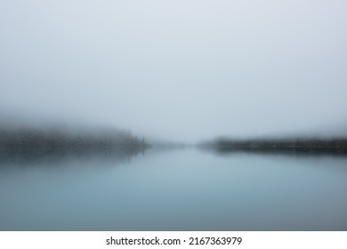 Tranquil meditative misty scenery of glacial lake with pointy fir tops reflection at early morning. Graphic EQ of spruce silhouettes on calm alpine lake horizon in mystery fog. Ghostly mountain lake. - Shutterstock ID 2167363979