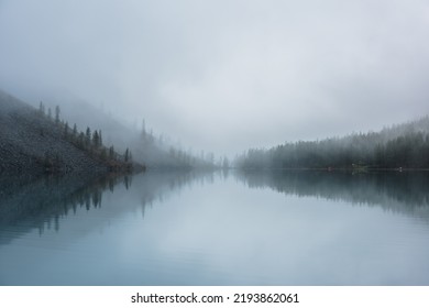 Tranquil meditative misty scenery of glacial lake with pointy fir tops reflection at early morning. Graphic EQ of spruce silhouettes on calm alpine lake horizon in mystery fog. Ghostly mountain lake.