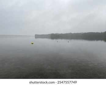 A tranquil, misty lake view on a foggy morning, featuring a calm water surface and a single yellow buoy. The soft, atmospheric setting captures the serenity of nature - Powered by Shutterstock