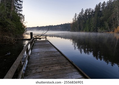 A tranquil morning scene at Elk Lake, with misty waters reflecting the sunrise glow. Surrounded by lush evergreen trees, the wooden pier invites moments of peace and contemplation. - Powered by Shutterstock