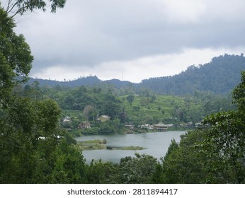 A tranquil mountain lake surrounded by lush green forests and rolling hills under dramatic overcast skies.