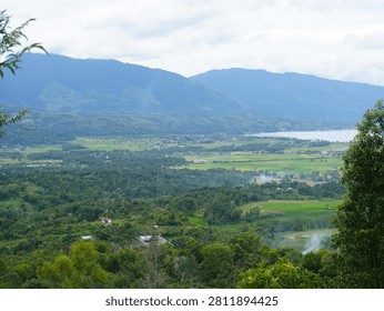 A tranquil mountain lake surrounded by lush green forests and rolling hills under dramatic overcast skies.