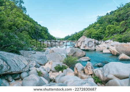 Tranquil natural scene with blue mountains, blue sky, and scattered rocks on the rippling river. Eco-tourism on a sunny day