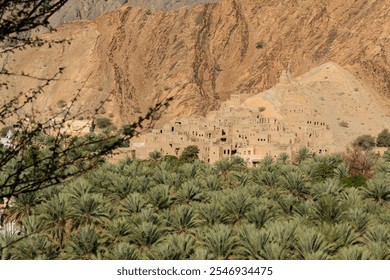 A tranquil oasis nestled in the mountains of Oman featuring lush palm trees and historic stone architecture - Powered by Shutterstock