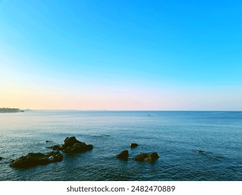 A tranquil ocean scene at sunset, with calm blue waters and a few rocky outcrops in the foreground. The sky transitions from a soft pastel gradient of blue to pink and orange. - Powered by Shutterstock