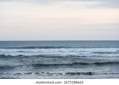 Tranquil ocean waves rolling toward the shore under a soft gradient sky transitioning from blue to pastel pink at dusk with a clear contrast line between sea and sky
