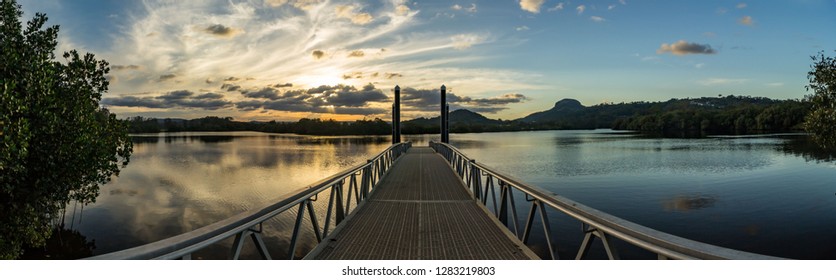 Tranquil panoramic Image of Jetty located at Lake Dunethan, Bli Bli Australia with a dramatic sky and the sun setting in the background. 