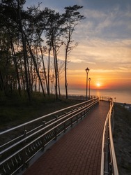 A Tranquil Pathway By The Coast At Sunset, Featuring Street Lamps, Trees, And A Picturesque Seascape.