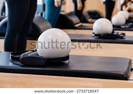 A tranquil Pilates studio interior featuring neatly arranged reformers, soft exercise balls, and supportive straps. Warm natural light fills the space, highlighting the clean, organized layout and inviting atmosphere. This serene setting embodies wellness, balance, and a commitment to holistic fitness, making it ideal for health, exercise, and lifestyle concepts.