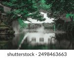 A tranquil pond with misty water in a Suzhou garden, where lush greenery meets a white wall and a stone archway.