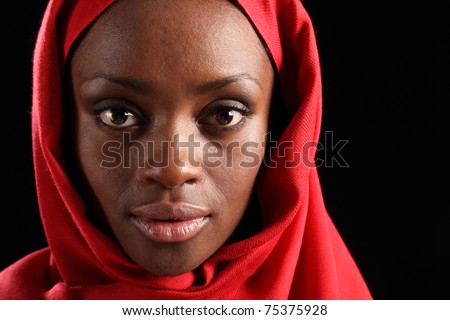 Tranquil portrait of beautiful young black african american woman wearing red hijab, taken against a black background.