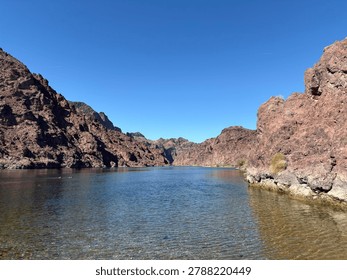 A tranquil river flows between rugged rocky cliffs under a clear blue sky.