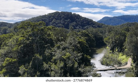 A tranquil river flows through dense green forests toward distant hills under a cloudy sky.