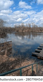 A tranquil river scene with reflections of clouds and trees, featuring a wooden dock and serene surroundings.