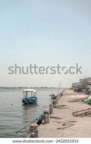 Tranquil riverside with moored boat and fishing rods, clear sky above.