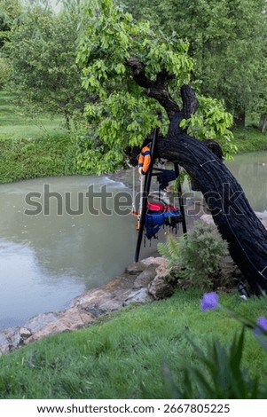 A tranquil riverside scene featuring a swing, life vests, and a leaning tree beside calm water at TakeTime Glamping, Saraburi, Thailand, on August 11, 2025.
