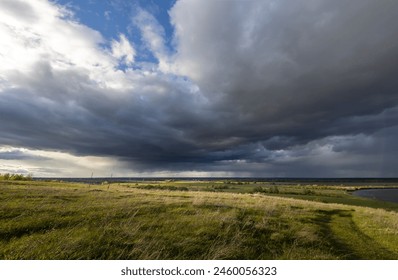 A tranquil rural landscape under a dramatic sky, where rolling hills of green grass meet a distant horizon under a mix of dark storm clouds and sunlight. - Powered by Shutterstock