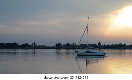 A tranquil sailboat floats on a serene lake at sunset, embodying relaxation and reflecting the concept of peaceful solitude - Powered by Shutterstock