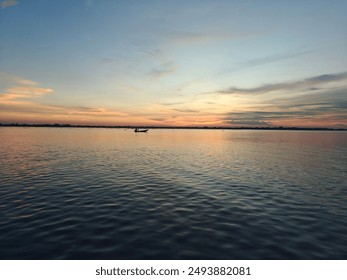 A tranquil scene at dusk, Orange colored dramatic sky with clouds reflecting in the lake water and a boat with human returning home. - Powered by Shutterstock