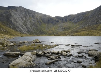 A tranquil scene at Lake Idwal in Snowdonia, Wales, featuring a rocky shoreline and steep green mountains, showcasing the natural beauty of the Welsh countryside. - Powered by Shutterstock