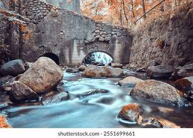 A tranquil scene of an old water mill, nestled amidst autumn foliage. The rushing water flows beneath the stone archway, creating a peaceful and picturesque setting. - Powered by Shutterstock