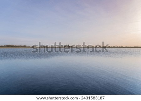 Tranquil scene over a dutch village lake with overflowing water Into the meadow. Sky above transitions from a warm palette of sunset hues to the cooler tones reflecting on the placid waters surface.