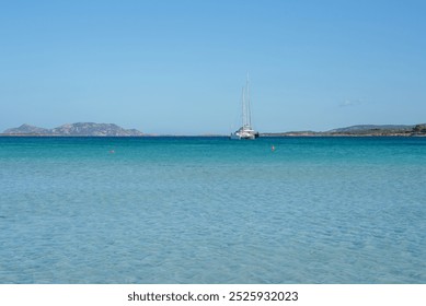 A tranquil scene in Sardinia featuring a solitary sailboat on calm turquoise waters, with low lying hills on the horizon and a clear sandy seabed visible. - Powered by Shutterstock