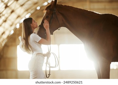 Tranquil scene, standing. Beautiful young woman is with horse indoors. - Powered by Shutterstock