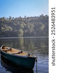 A tranquil scene unfolds as a small canoe rests peacefully on the still waters of a serene lake, surrounded by lush greenery.