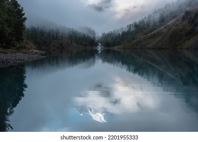 Tranquil Scenery With Reflex In Mountain Lake Of Snow Castle In Clouds. Snowy Mountains In Fog Clearance, Small River And Coniferous Trees Reflected In Alpine Lake. Mountain Creek And Glacial Lake.