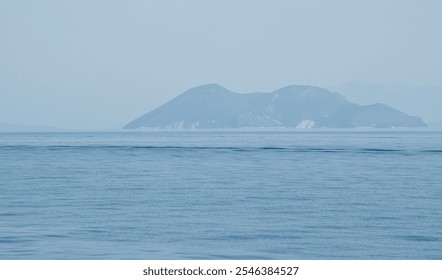 Tranquil seascape featuring a small island in the distance, creating a serene and minimalist composition. Ithace greek Island Greece - Powered by Shutterstock