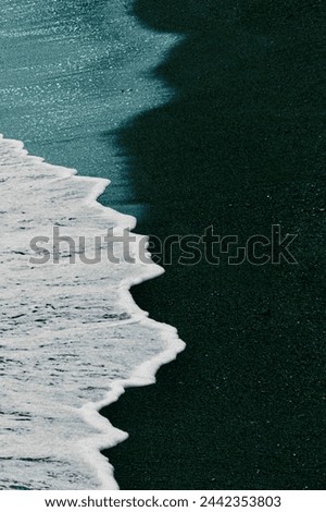 A tranquil seascape where gentle waves caress the dark sandy shore, creating a harmonious dance of white sea foam and shadowed sand textures, ideal for themes of peace and natural elegance.