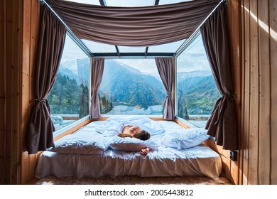 Ruhige, ruhige Frau, die auf einem weichen, weißen, gemütlichen, warmen Bett im Zimmer mit Aussicht auf die Berge schläft