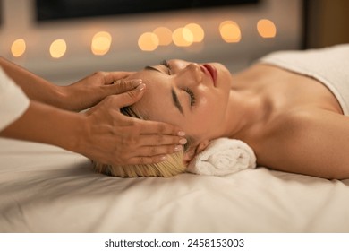 In a tranquil spa environment, a young woman with blonde hair experiences a soothing facial massage, radiating relaxation and peace. - Powered by Shutterstock